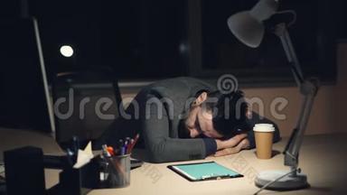 一个穿西装的疲惫的家伙，在忙碌的工作日后，深夜睡在办公室的办公桌上。 打开电脑，外卖